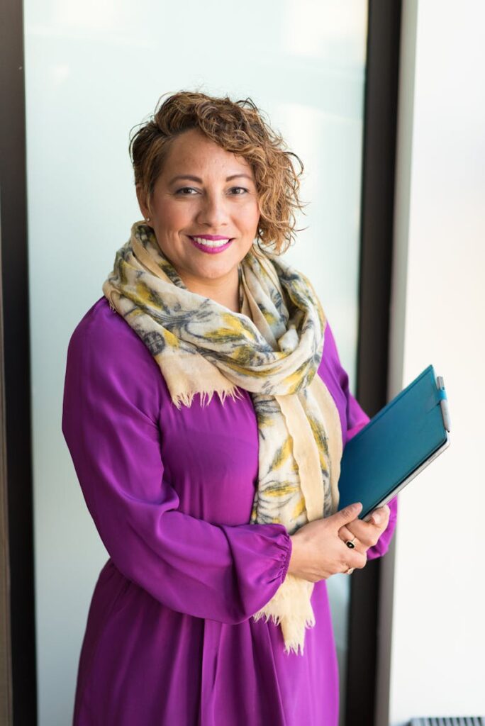 Smiling woman in a purple dress and scarf holding a tablet indoors.